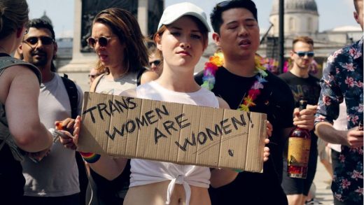 An image of a woman holding a cardboard sign reading 'trans women are women'